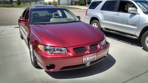 2002 Pontiac Grand Prix - A red 2002 Pontiac Grand Prix is parked next to a silver SUV, showing its front 3/4 profile and sunroof.