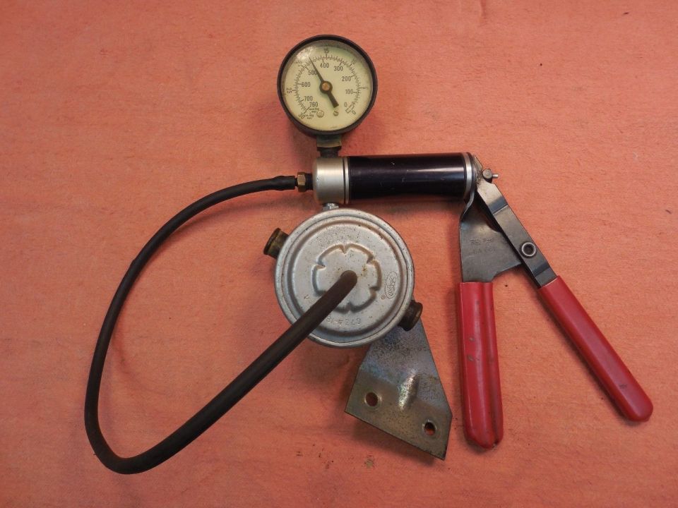 Fuel pressure regulator with attached gauge and hose, next to a red-handled tool