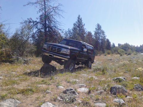1995 Ford Bronco - A dark-colored Ford Bronco navigates rocky terrain under a clear blue sky.