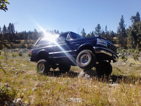 1995 Ford Bronco - A black Ford Bronco navigates rocky terrain with its front-right tire high off the ground.