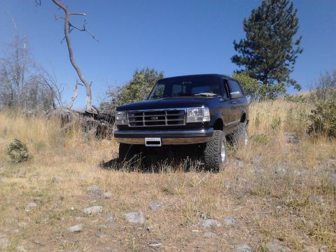 1995 Ford Bronco - This black 1995 Ford Bronco is parked on a dry, grassy hill under a clear blue sky.