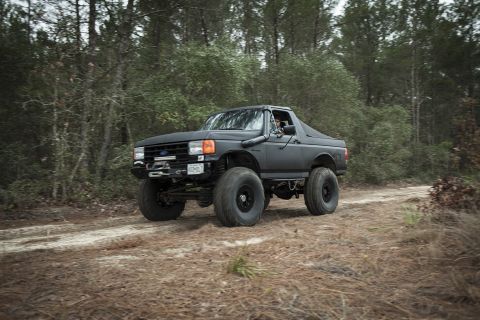 1989 Ford Bronco - This lifted 1989 Ford Bronco, equipped with a snorkel, navigates a wooded dirt path.