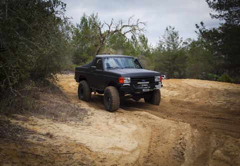 1989 Ford Bronco - Modified 1987 Ford F-150 truck navigating a dirt path in a wooded area.
