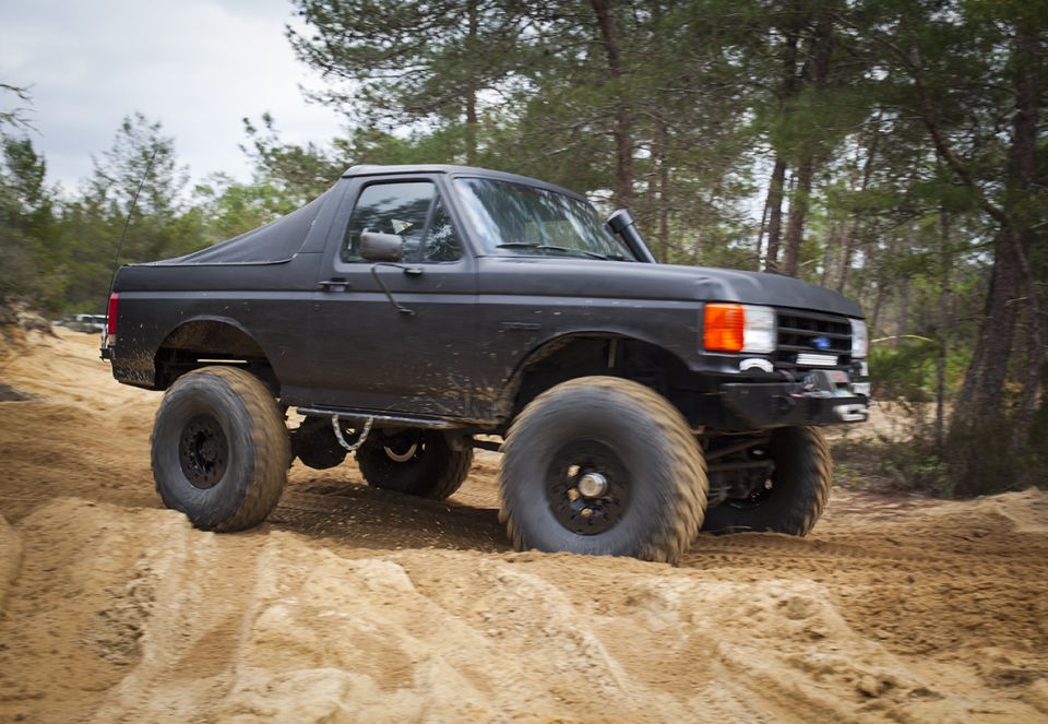 Black Ford Bronco with large tires driving on a sandy trail through trees