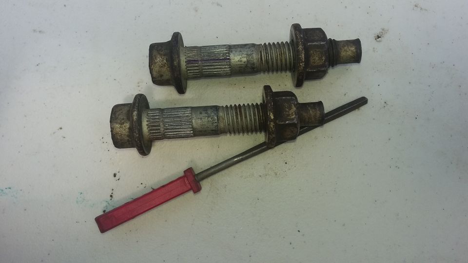 Two lug bolts with nuts and a red-handled tool on a white surface