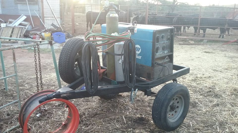 Welding machine with Miller logo on a trailer with two tires, propane tank, and cables. A red rim is visible