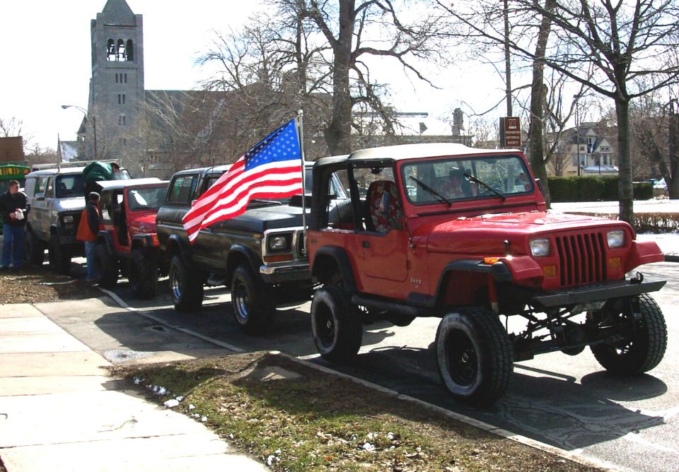 Lifted red Jeep Wrangler flying an American flag leads a line of 4x4s parked by a church