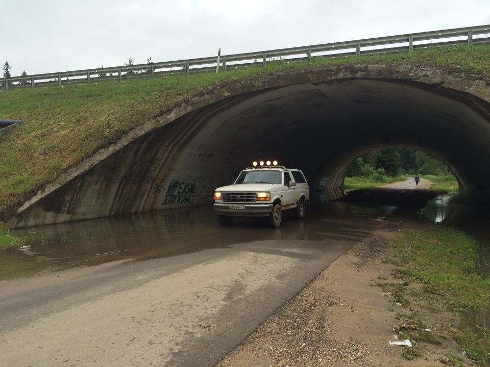 White 1993 Ford Bronco with roof lights driving through a flooded underpass.