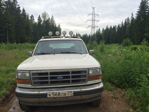 1993 Ford Bronco - A white Ford Bronco is parked on a dirt road in a wooded area with a power line tower in the background. The vehicle has a roof-mounted lig…