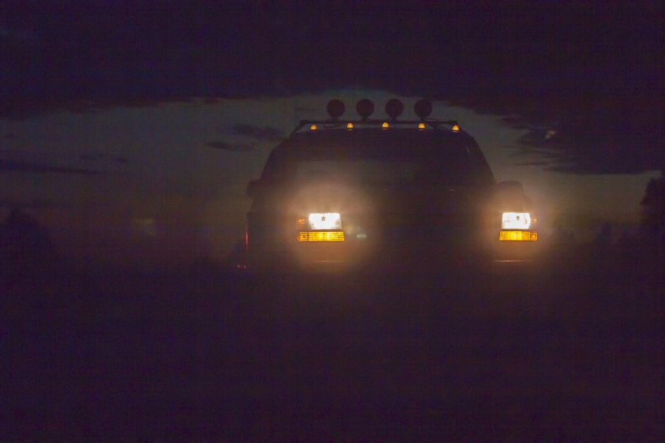 Front view of a dark SUV at night with headlights and roof lights on.