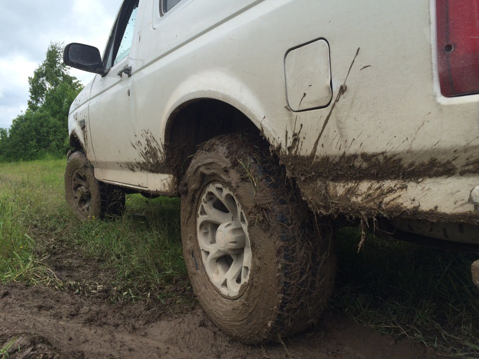 Mud-covered white 1993 Ford Bronco, rear 3/4 view, low angle.