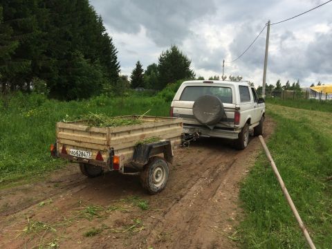 1993 Ford Bronco - A white Ford Bronco is parked on a muddy dirt road next to a trailer filled with cut grass. The vehicle has a spare tire mounted on the bac…