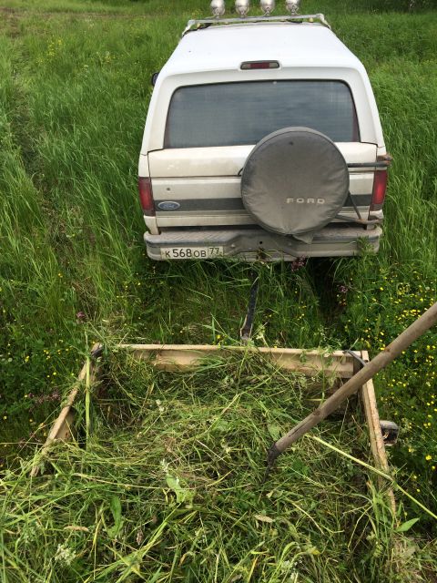1993 Ford Bronco - The rear of a white 1993 Ford Bronco is visible, parked in a grassy field. A wooden frame filled with cut grass sits in the foreground, wit…