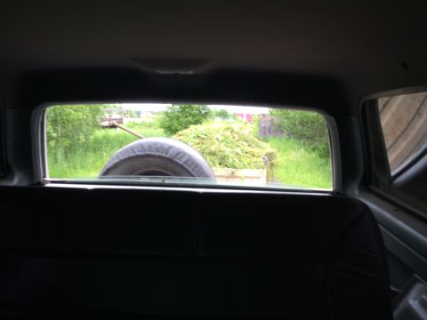 1993 Ford Bronco - View from the interior of a vehicle looking out the rear window at a trailer loaded with hay. A spare tire is visible in the foreground, mo…