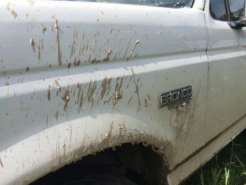 1993 Ford Bronco - The side panel of a white Ford Bronco is heavily splattered with mud. A "BRONCO" emblem is visible on the door.