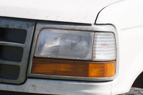 1993 Ford Bronco - Close-up of the front passenger side headlight and amber turn signal on a white 1993 Ford Bronco. The vehicle appears dusty and shows signs…