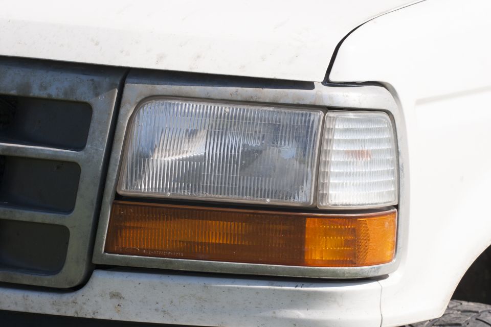 Front passenger side headlight and amber turn signal on a dusty white 1993 Ford Bronco.
