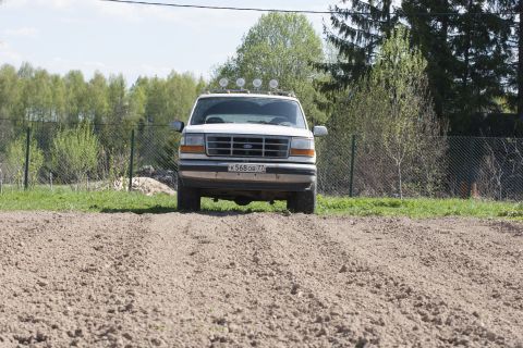 1993 Ford Bronco - A white Ford Bronco is parked on a dirt patch in front of a chain-link fence and trees. The vehicle has four auxiliary lights mounted on th…