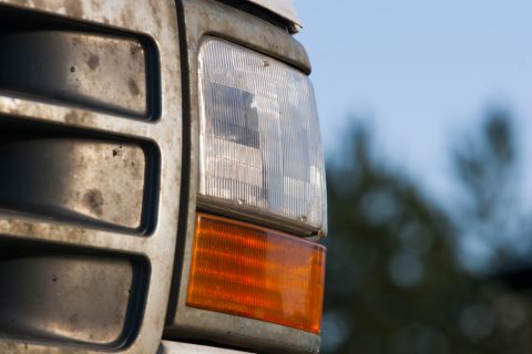 1993 Ford Bronco - A close-up, right-side view of a dirty, weathered headlight and orange turn signal on the front of a vehicle. The vehicle's grille is visib…