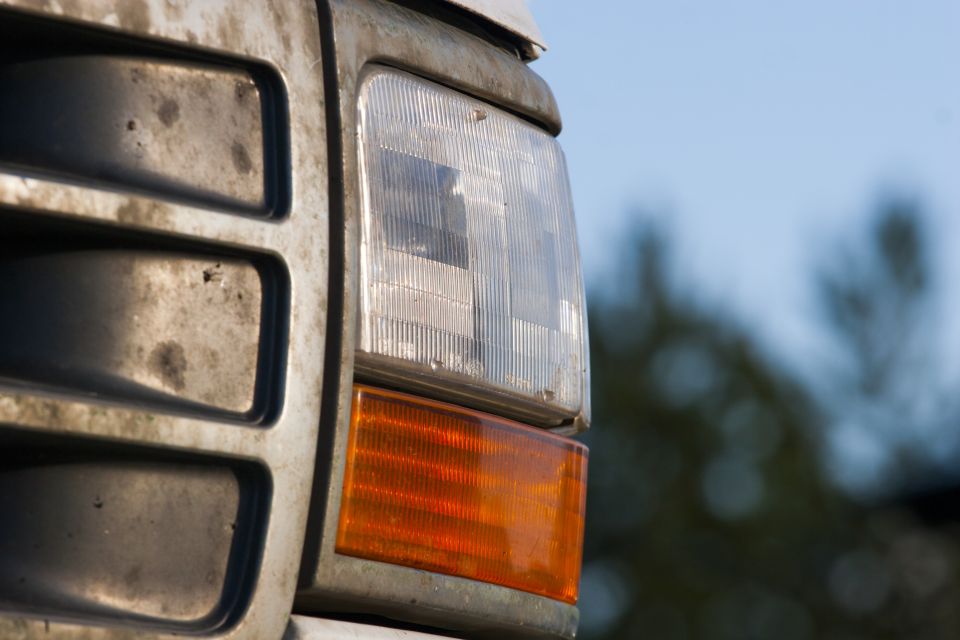 Close-up of a dirty vehicle headlight and orange turn signal with grille detail.