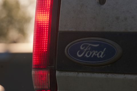 1993 Ford Bronco - The rear of a vehicle shows a red taillight and the oval Ford emblem on a dusty surface. The emblem has the word "Ford" in white script.