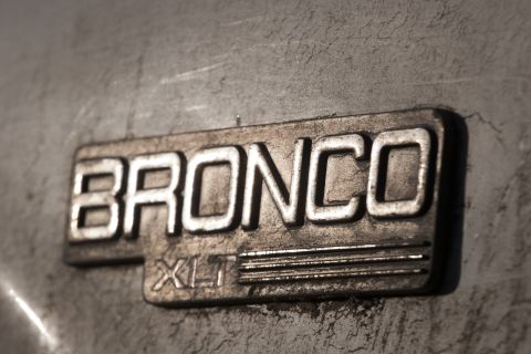 1993 Ford Bronco - A close-up shot shows the embossed "BRONCO" and "XLT" badging on a textured, metallic surface. The lighting highlights the raised lettering…