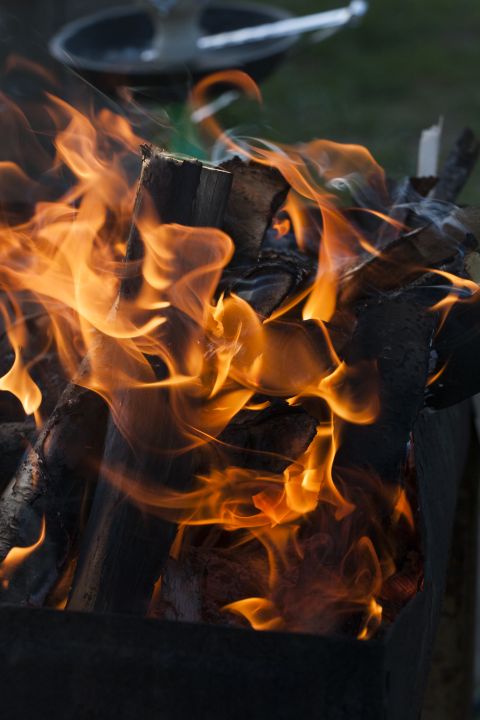 1993 Ford Bronco - Flames engulf burning logs within a dark metal fire pit. The fire is bright orange and yellow, with wisps of smoke curling upwards.