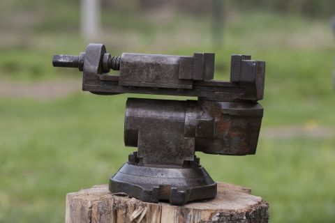 1993 Ford Bronco - A close-up, side-view of a rusted, metal vise with a rotating base sits on a wooden stump. The background is a blurred green field.