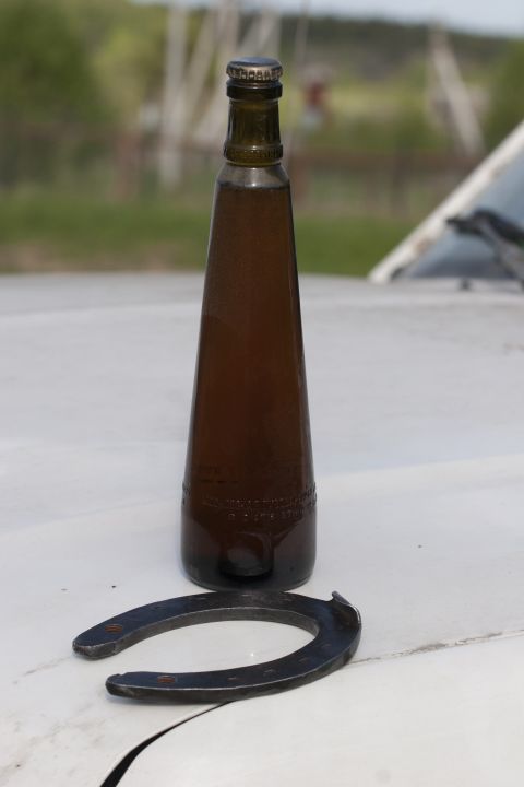 1993 Ford Bronco - A brown glass bottle filled with a dark liquid sits on a white surface next to a metal horseshoe. The bottle has embossed text near its bas…