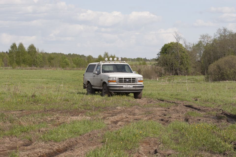 White 1993 Ford Bronco with roof lights in a grassy field.