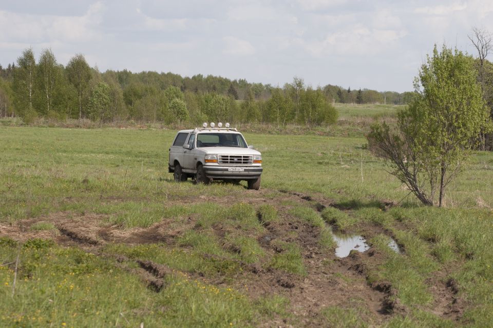 White 1993 Ford Bronco in a grassy field with tire tracks.