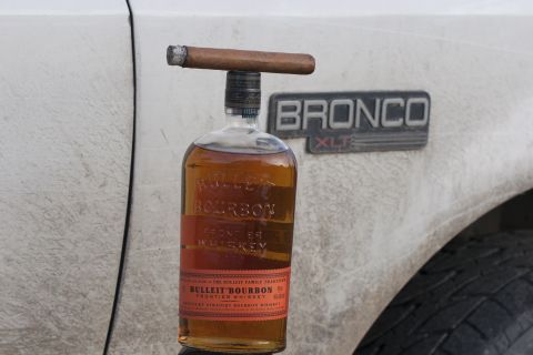 1993 Ford Bronco - A bottle of Bulleit Bourbon Frontier Whiskey is balanced on top of a cigar, which is resting on the cap of the bottle. The bottle and cigar…