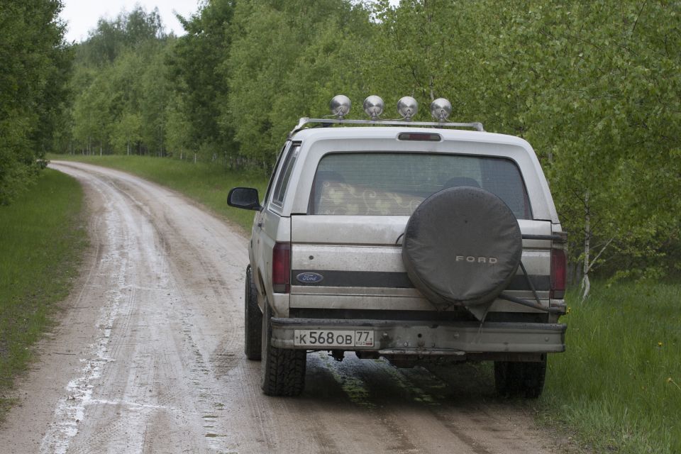 Silver Ford Bronco parked on a wet dirt road with trees on the side.