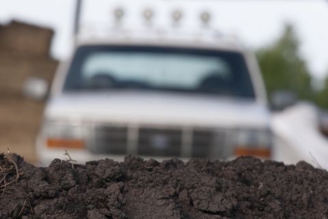 1993 Ford Bronco - The rear of a white SUV is visible, blurred behind a pile of dark soil in the foreground. The SUV has four lights mounted on its roof.