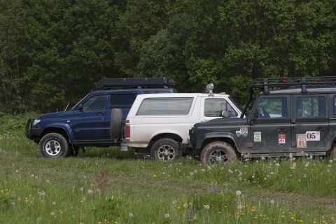 1993 Ford Bronco - Three off-road vehicles are parked side-by-side in a grassy field with trees in the background.