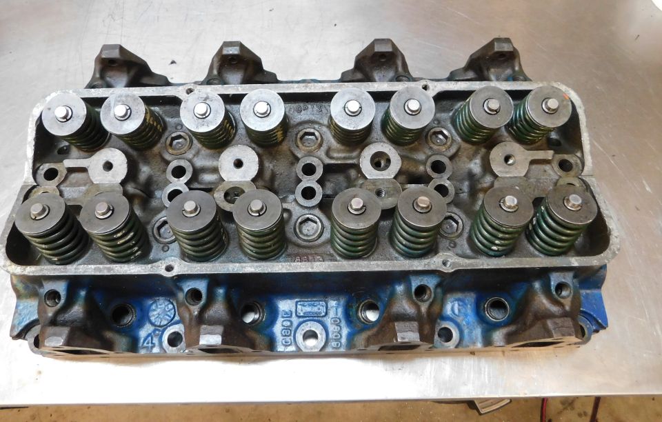Overhead view of a blue V8 engine cylinder head with valve springs and retainers.