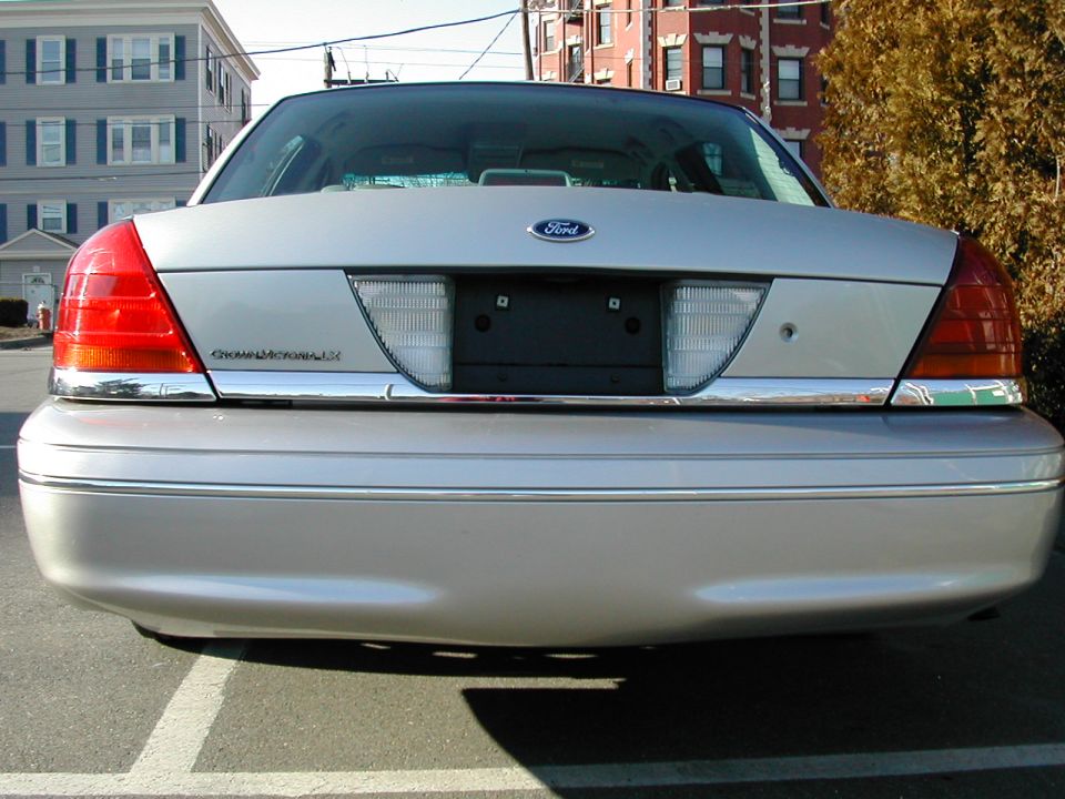 Rear view of silver Ford Crown Victoria LX sedan with no license plate, parked near brick buildings