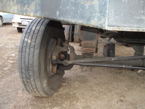 1987 Ford Bronco - Close-up view of the front wheel suspension and leaf springs on a truck, with another vehicle visible in the background.