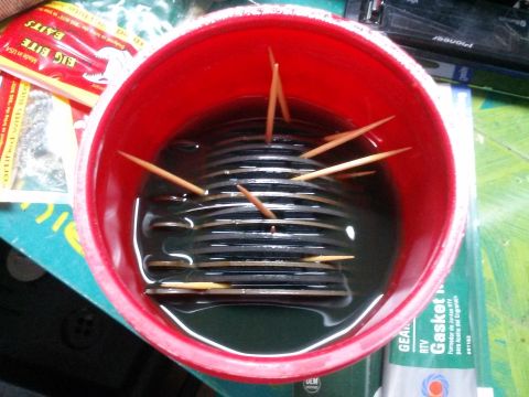 1996 Ford Bronco - A red plastic bucket filled with dark liquid and several toothpicks sticking out of a stack of black circular objects. A package of fishing…