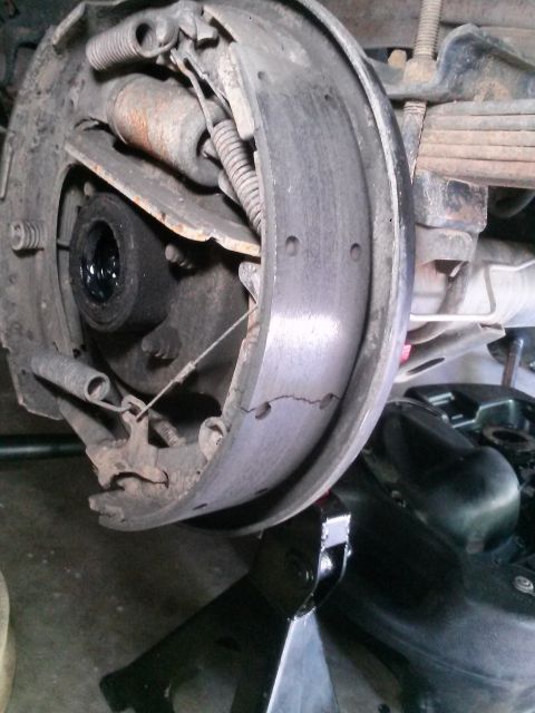 1996 Ford Bronco - A close-up view of a cracked brake shoe and drum assembly on a vehicle, supported by a jack stand. The brake components appear worn and dus…