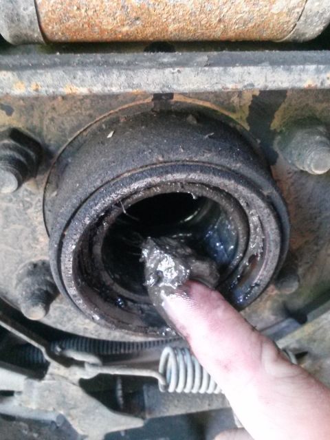 1996 Ford Bronco - A close-up view shows a finger covered in thick, black grease being inserted into a heavily greased wheel bearing assembly, likely from a 1…