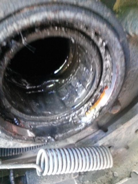1996 Ford Bronco - A close-up view of a heavily corroded and greasy internal component, possibly a wheel bearing assembly, with a large coil spring visible in…