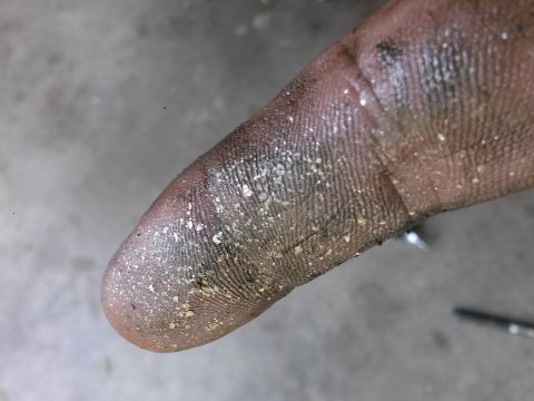 1996 Ford Bronco - A close-up shot shows a dirty finger covered in dust and small particles, resting on a gray, textured surface.
