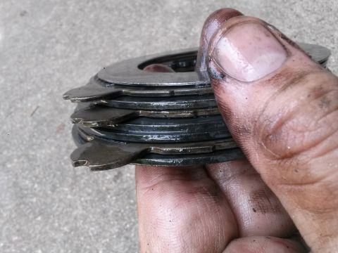 1996 Ford Bronco - A close-up shot shows a stack of wet, metallic clutch plates being held by a greasy hand. The plates have a unique shape with notches aroun…