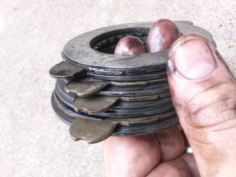 1996 Ford Bronco - A stack of metal clutch plates, some with tabs, are held by a hand with dirty fingers. The plates appear to be wet or oily.