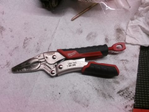 1996 Ford Bronco - A pair of red and silver Milwaukee locking pliers with black grips are lying on a white surface with some dark smudges. The pliers have "TO…