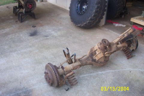 1979 Ford F-150 - A rusty rear axle assembly is on the ground, with a large tire visible in the background.