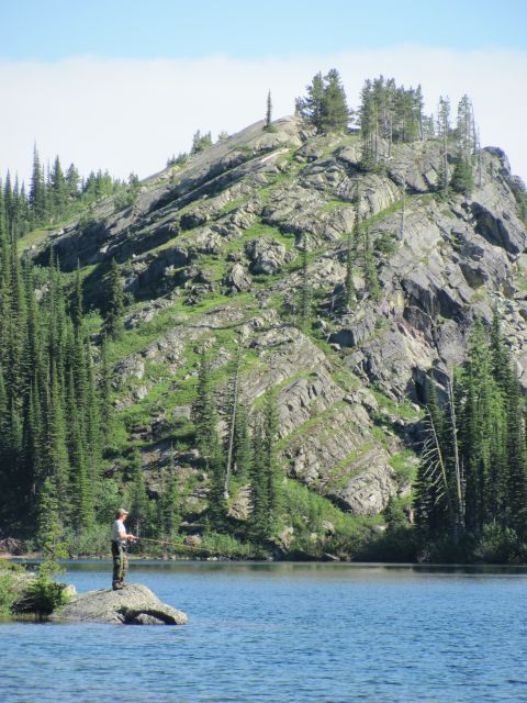 1974 Ford Ranchero - A person fishes from a rock in a lake with a large, rocky, tree-covered hill in the background.
