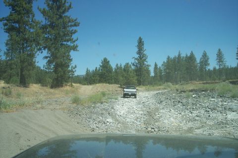 1995 Ford Bronco - A lone SUV travels down a dusty, unpaved road under a clear blue sky.
