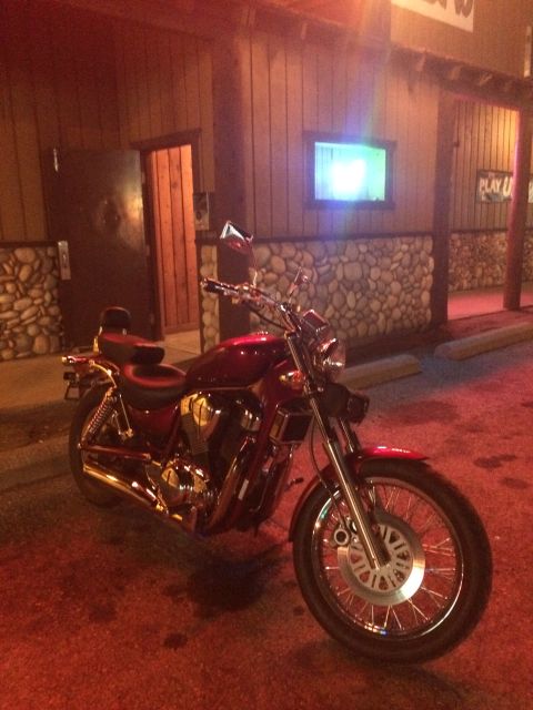 1974 Ford Ranchero - A red motorcycle is parked in front of a building with a stone facade and wood paneling. The motorcycle has chrome accents and spoked wheel…
